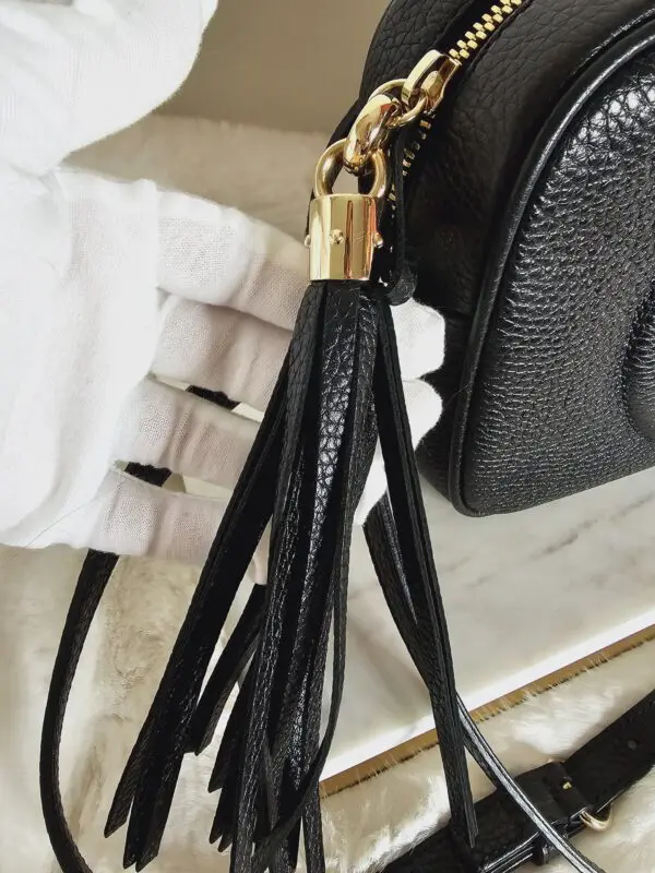 A black purse with a gold chain and tassel.