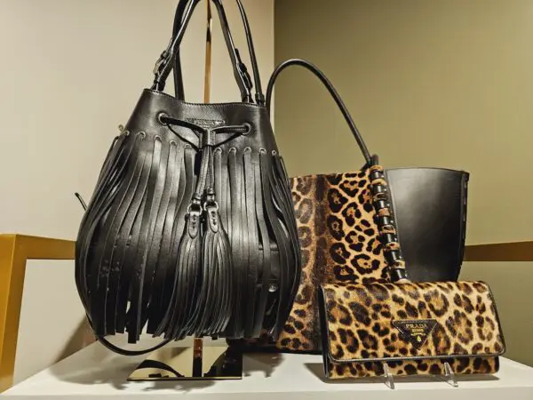 A black purse sitting on top of a counter next to leopard print bags.