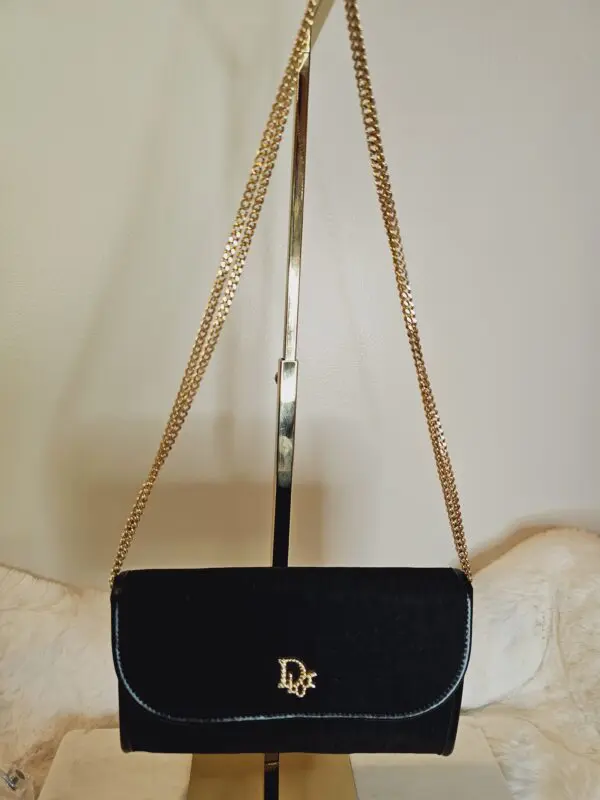 A black purse with gold chain strap hanging on the wall.