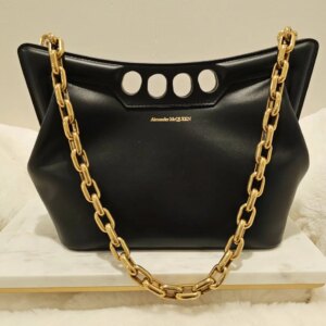 A black purse with gold chain on top of white marble.