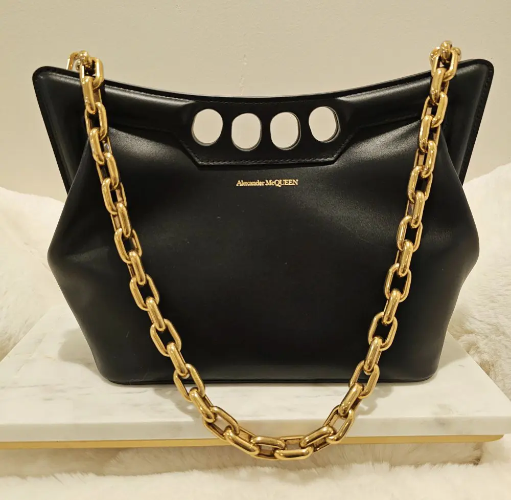 A black purse with gold chain on top of white marble.