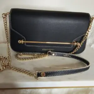 A black purse with gold chain strap and a metal bar.