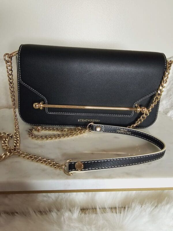 A black purse with gold chain strap and a metal bar.