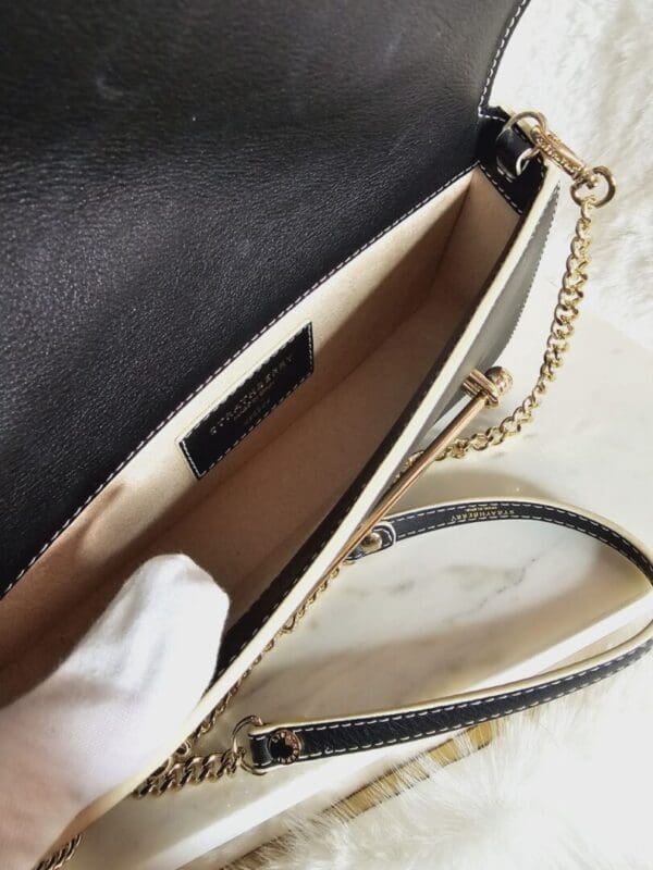 A black purse with gold chain and white leather.