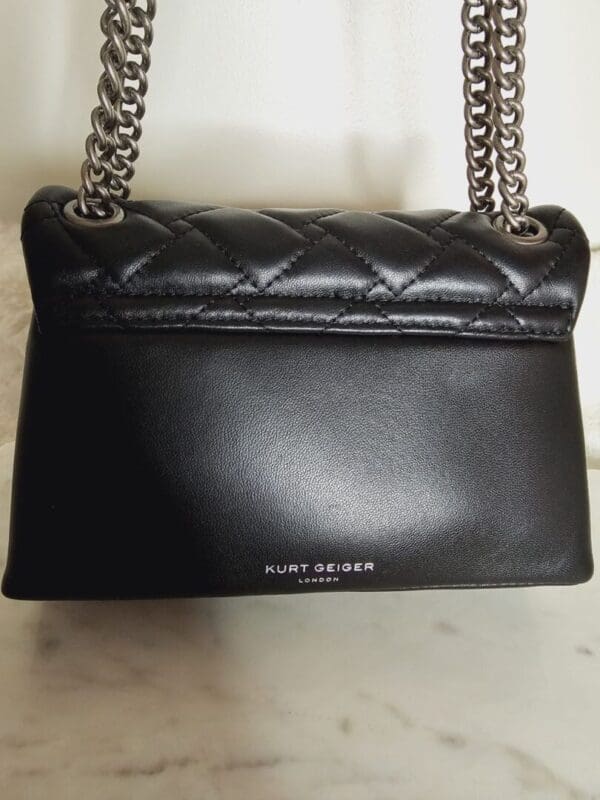 A black purse with silver chain straps on top of the floor.