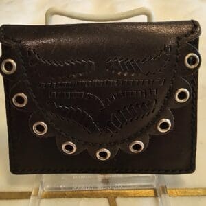 A black purse with white eyelets on top of a stand.