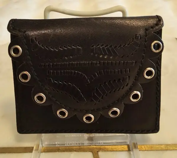 A black purse with white eyelets on top of a stand.