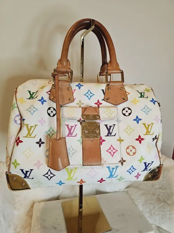 A white purse with multi colored handles and a brown leather strap.