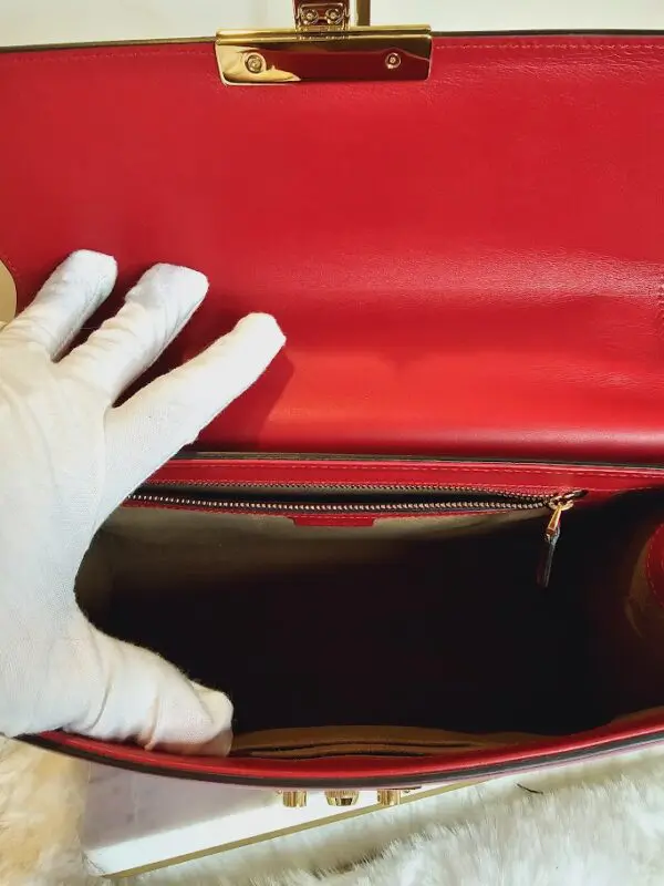 A person wearing white gloves and holding onto a red purse.