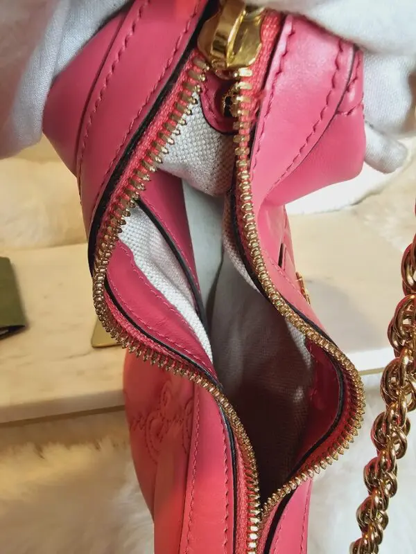 A pink purse is open and has a chain strap.