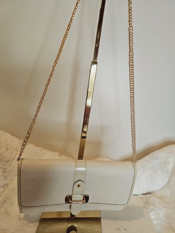 A white purse with gold chain strap hanging on the wall.