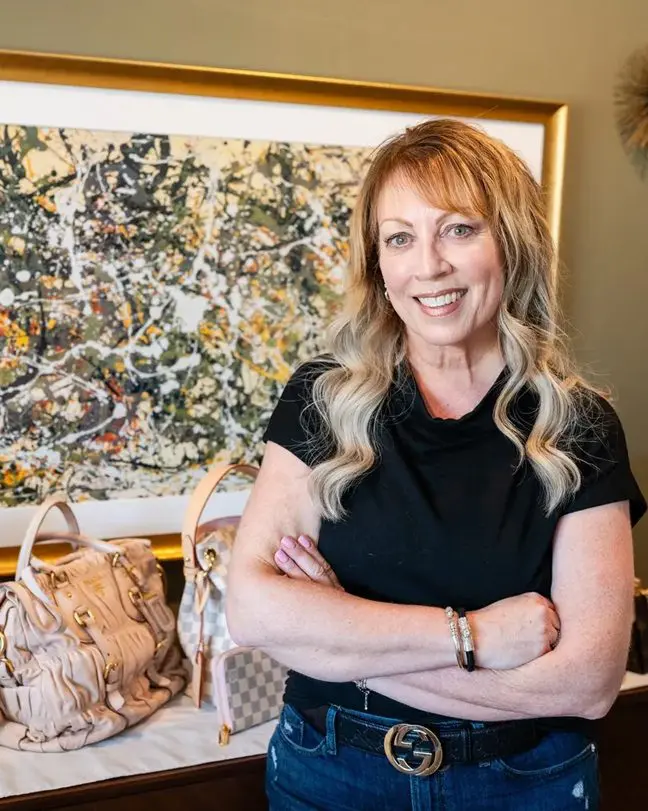 A woman standing in front of a painting and purse.